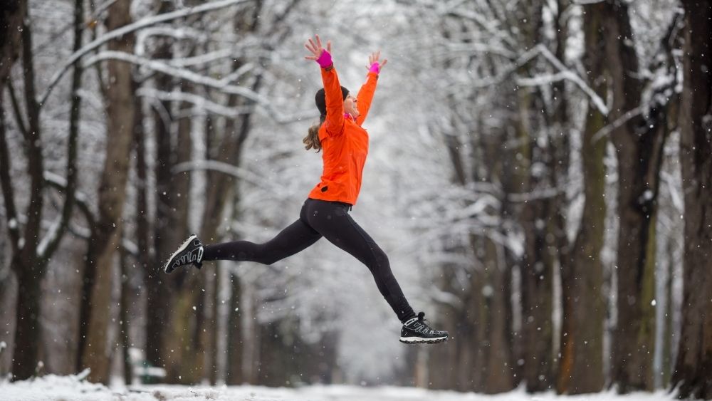 冬景色を背景にジャンプする女性