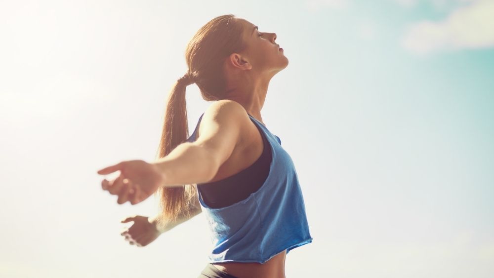 青空の下、両手を広げて気持ちよさそうに深呼吸をしているスポーツウェア姿の女性
